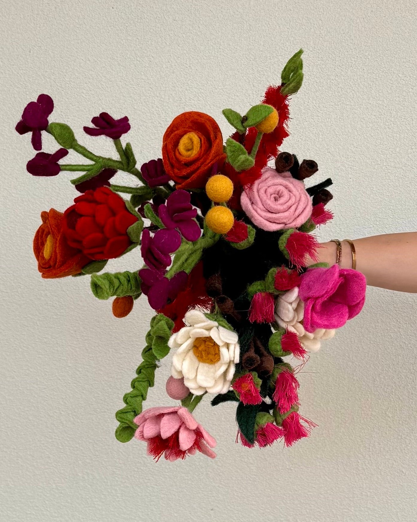 a bunch of colourful felt flowers being held by a hand
