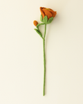 A single felt flower stem with an orange rose bud, green leaves, and a long green stem, photographed against a plain off-white background.