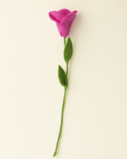 A single felt flower decoration with a pink-purple bloom, green stem, and two green leaves, photographed on a plain warm off-white background.