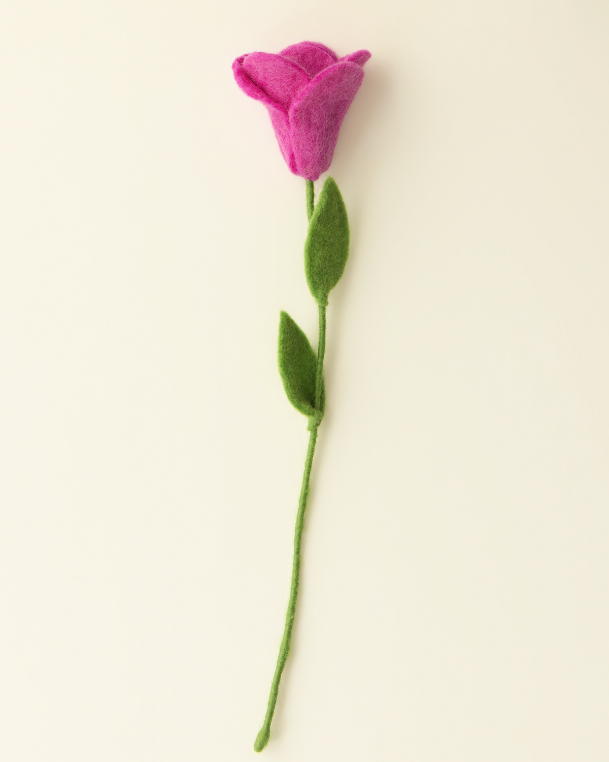 A single felt flower decoration with a pink-purple bloom, green stem, and two green leaves, photographed on a plain warm off-white background.